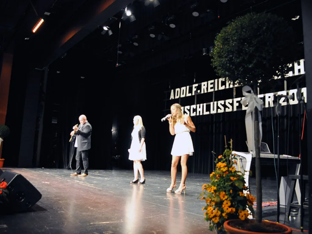 Personen singen an Mikrofonen auf der Bühne.